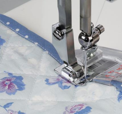 A Janome taping foot attachment stitching a narrow blue fabric tape binding onto a quilt.
