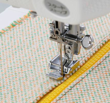A Janome zipper foot attachment stitching right alongside a yellow zipper on patterned fabric.