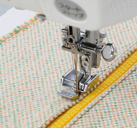 A Janome zipper foot attachment stitching right alongside a yellow zipper on patterned fabric.