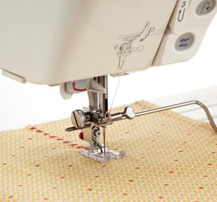 A metal Janome long quilting guide bar attached to a machine head tracing a fabric seam line.