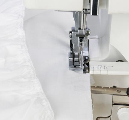 A Janome serger gathering attachment processing ruffles on white fabric under the presser foot.