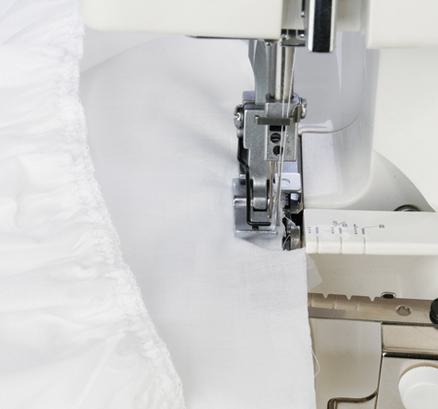 A Janome serger gathering attachment processing ruffles on white fabric under the presser foot.