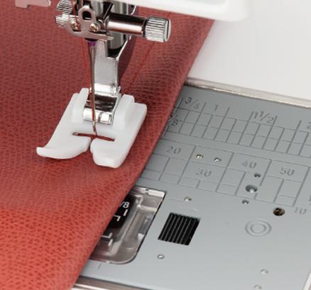 A white Janome ultraglide non-stick presser foot stitching along a strip of brown leather.