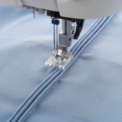 A multi-line decorative stitch presser foot with clear alignment guides sewing light fabric.